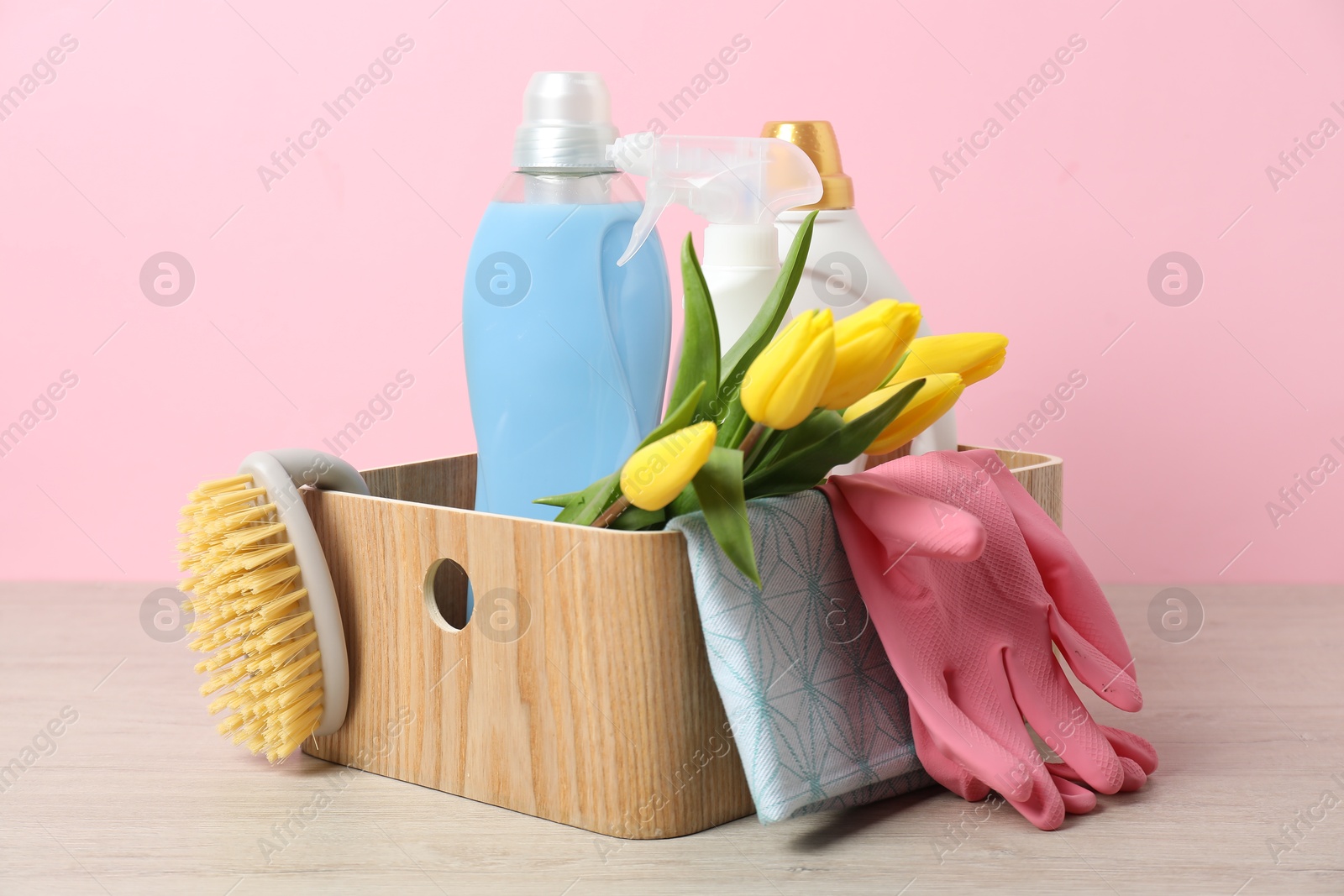 Photo of Spring cleaning. Detergents, supplies and tulips on white wooden table against pink background