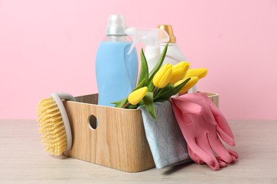 Photo of Spring cleaning. Detergents, supplies and tulips on white wooden table against pink background