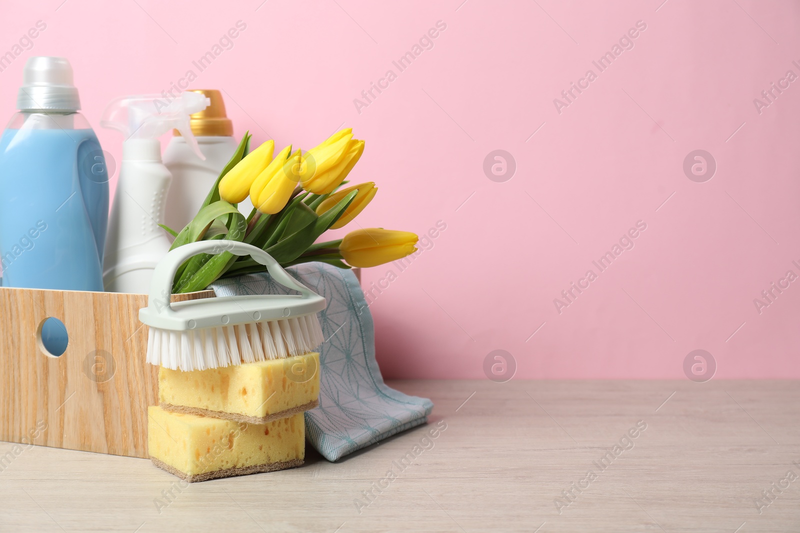 Photo of Spring cleaning. Detergents, supplies and tulips on white wooden table against pink background, space for text