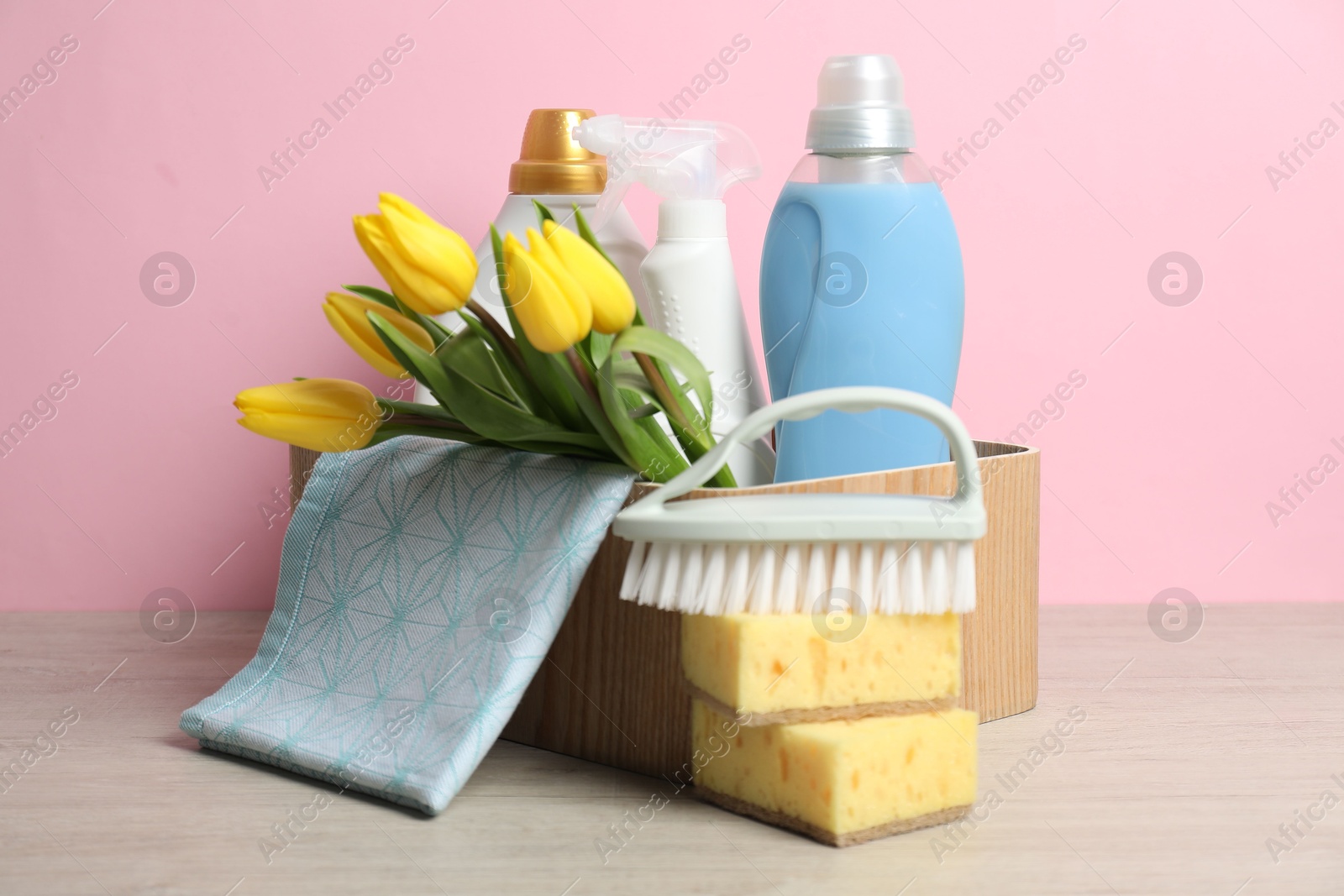 Photo of Spring cleaning. Detergents, supplies and tulips on white wooden table against pink background