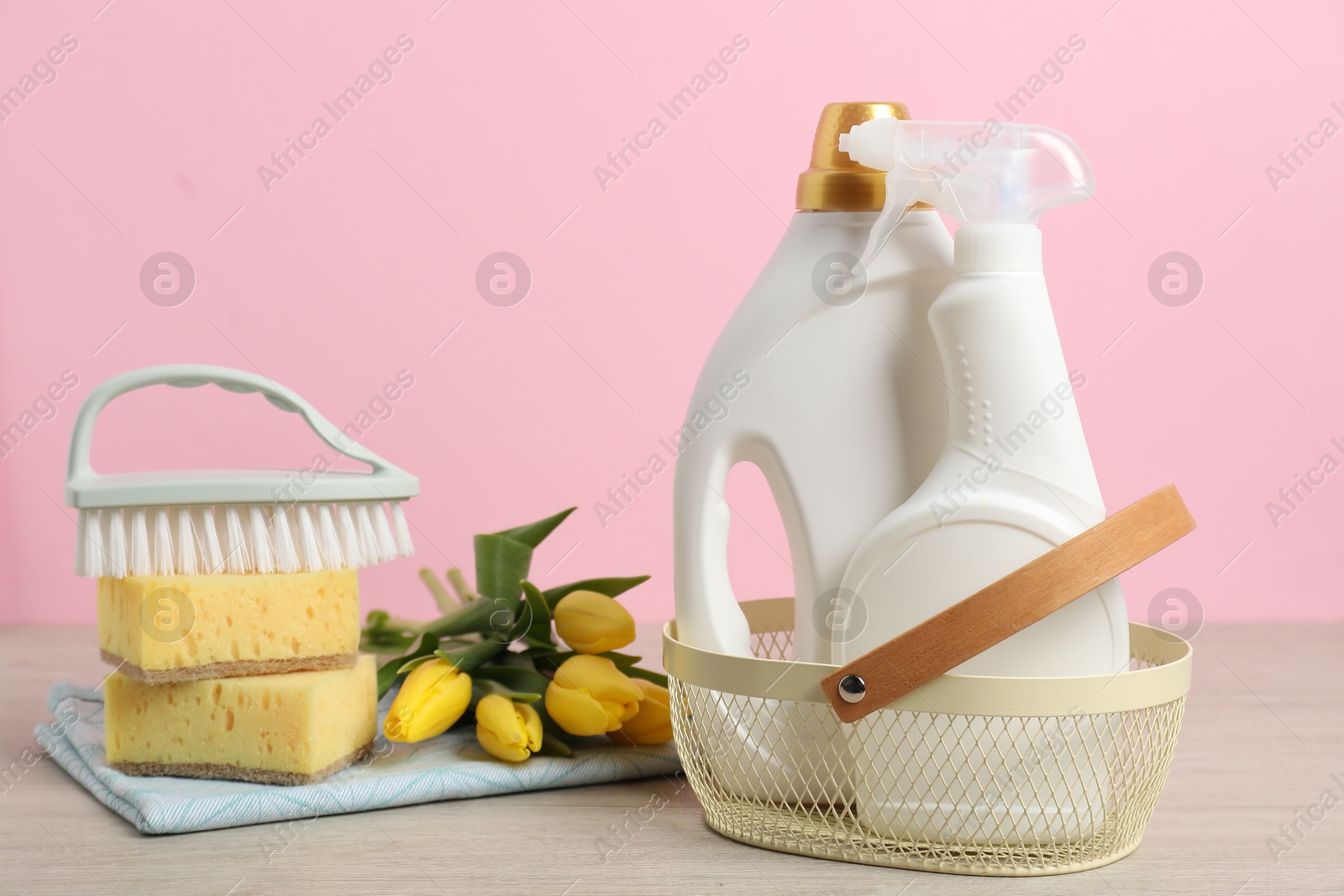 Photo of Spring cleaning. Detergents, supplies and tulips on white wooden table against pink background