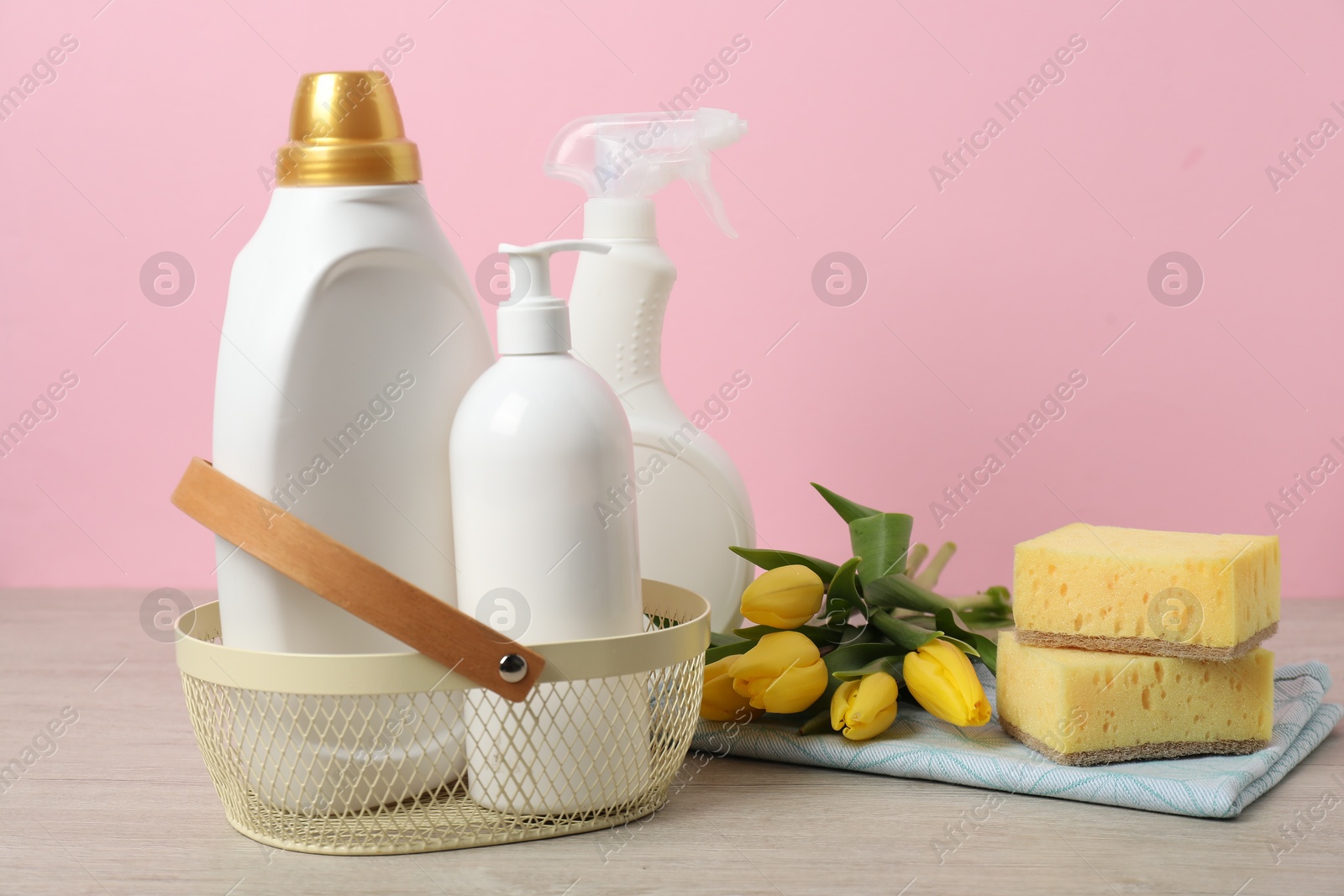 Photo of Spring cleaning. Detergents, supplies and tulips on white wooden table against pink background