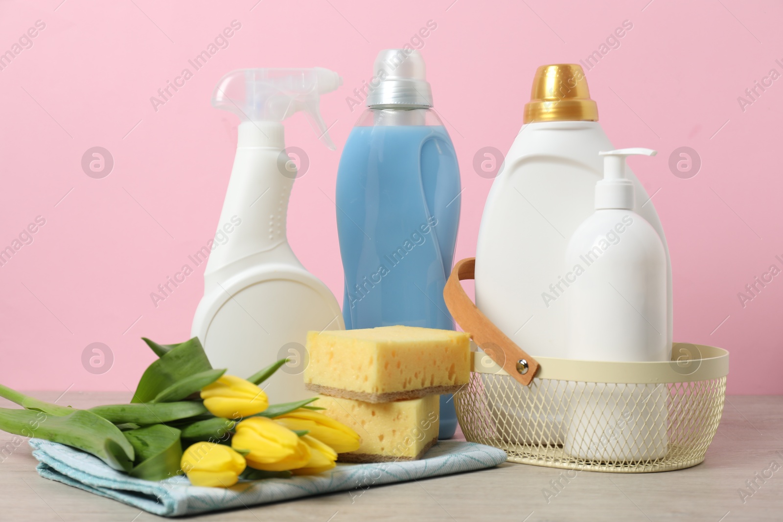 Photo of Spring cleaning. Detergents, supplies and tulips on white wooden table against pink background