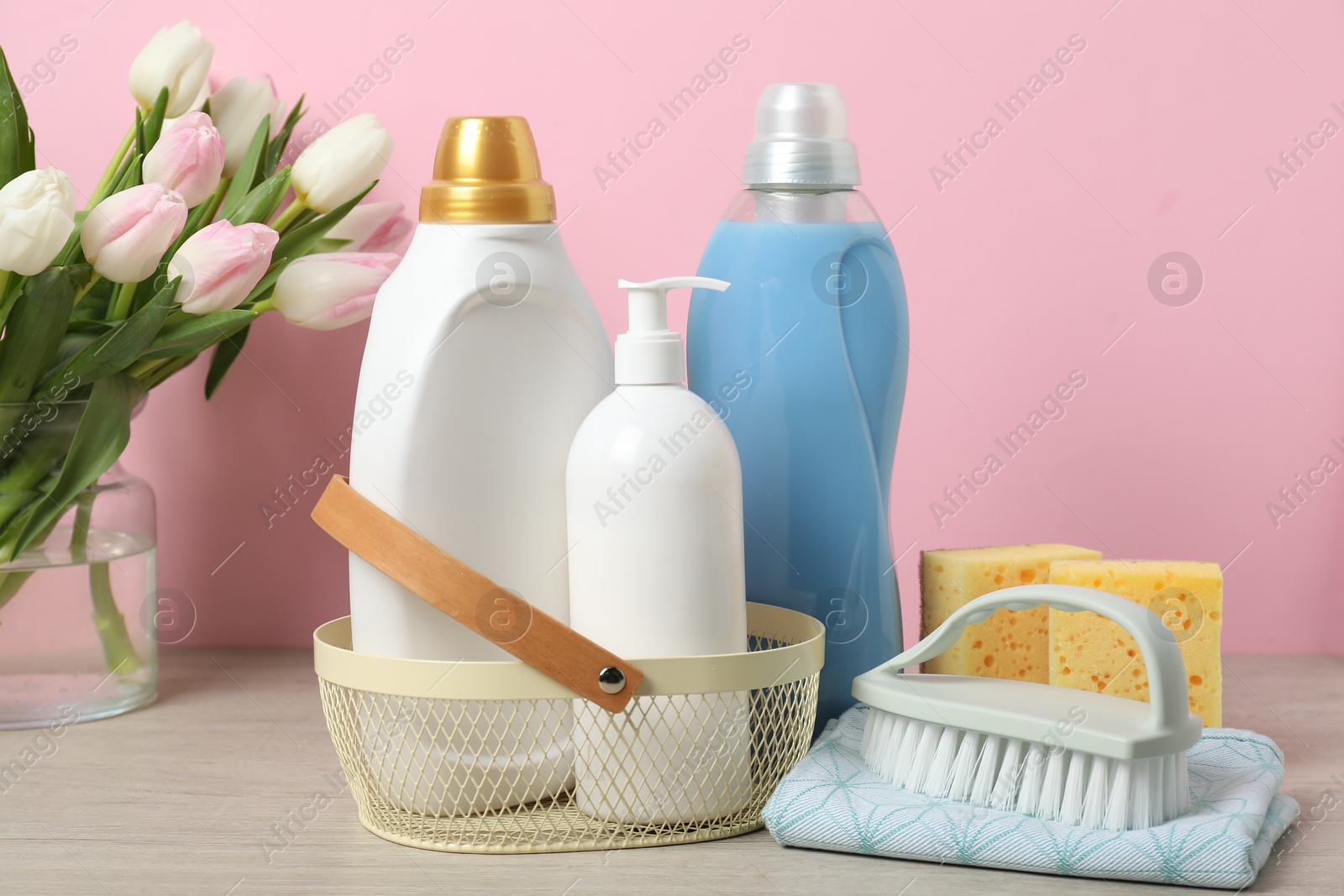 Photo of Spring cleaning. Detergents, supplies and tulips on white wooden table against pink background