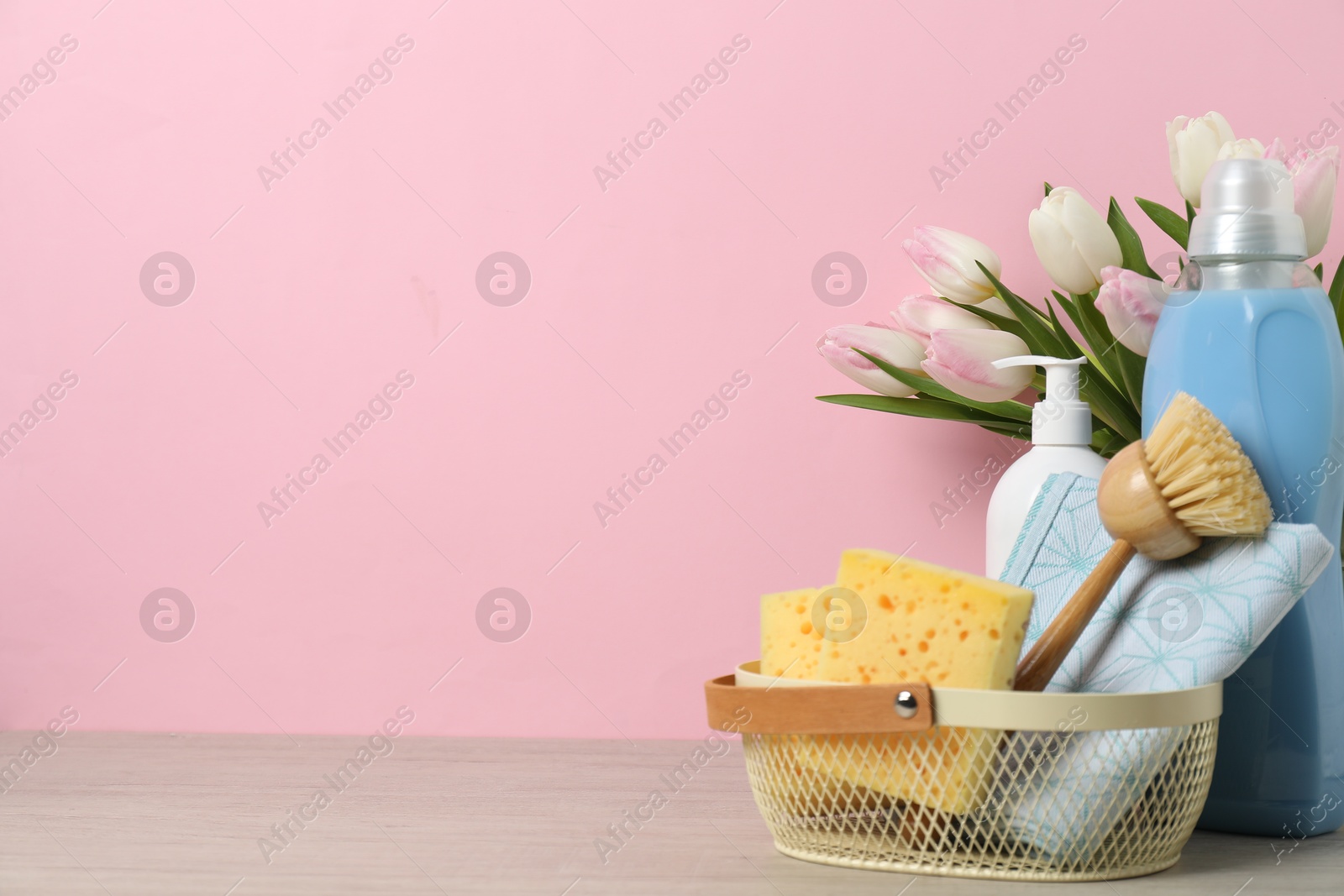 Photo of Spring cleaning. Detergents, supplies and tulips on white wooden table against pink background, space for text