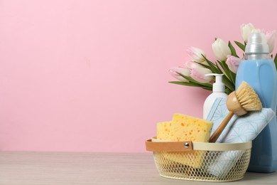 Photo of Spring cleaning. Detergents, supplies and tulips on white wooden table against pink background, space for text