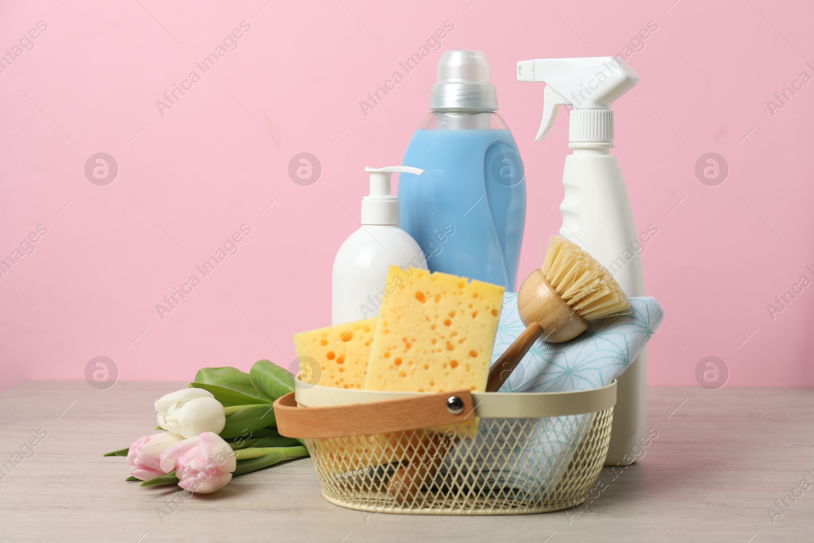 Photo of Spring cleaning. Detergents, supplies and tulips on white wooden table against pink background