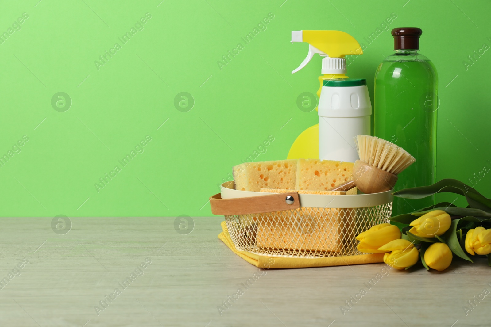 Photo of Spring cleaning. Detergents, supplies and tulips on white wooden table against green background, space for text