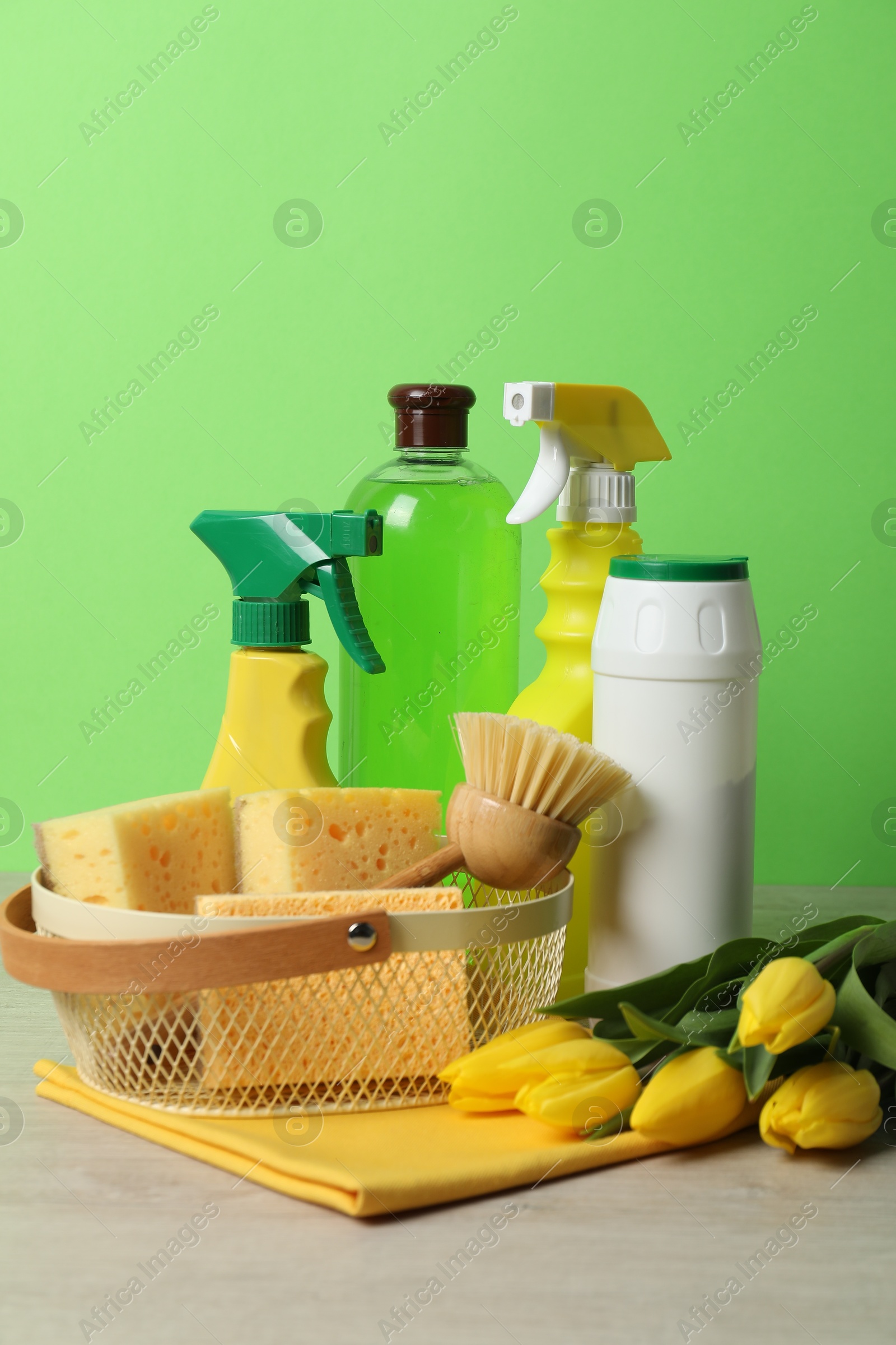 Photo of Spring cleaning. Detergents, supplies and tulips on white wooden table against green background