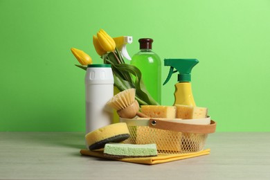 Photo of Spring cleaning. Detergents, supplies and tulips on white wooden table against green background