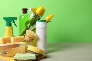 Photo of Spring cleaning. Detergents, supplies and tulips on white wooden table against green background, space for text