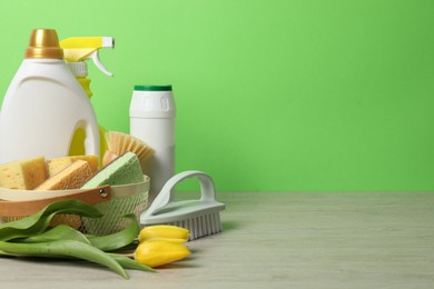 Photo of Spring cleaning. Detergents, supplies and tulips on white wooden table against green background, space for text