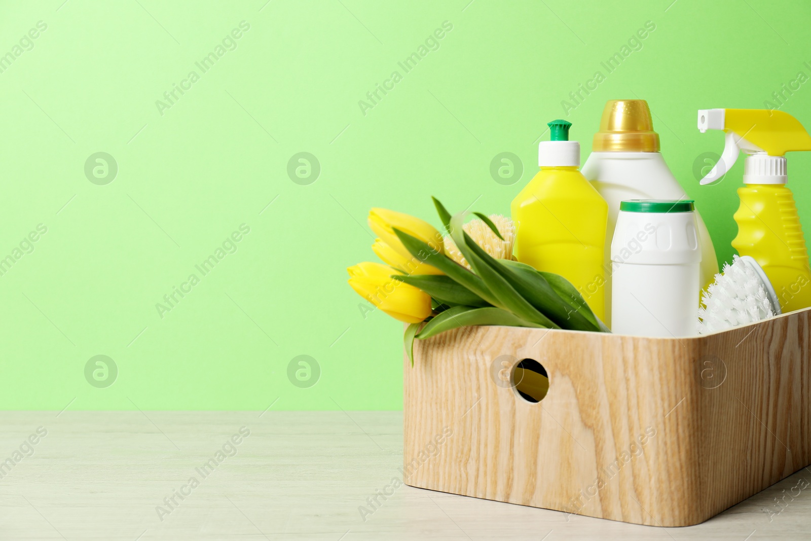 Photo of Spring cleaning. Detergents, supplies and tulips on white wooden table against green background, space for text