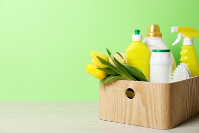 Photo of Spring cleaning. Detergents, supplies and tulips on white wooden table against green background, space for text