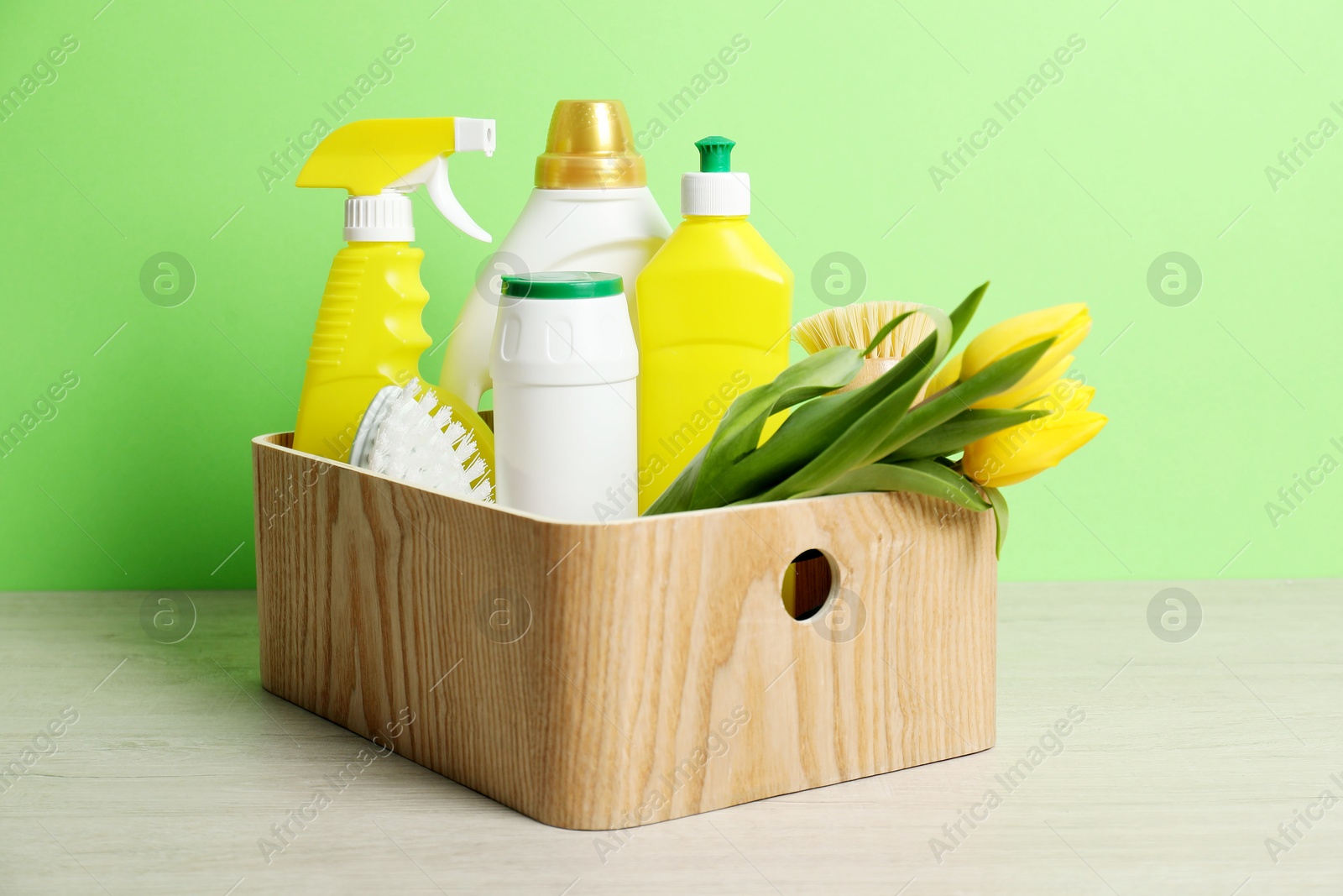 Photo of Spring cleaning. Detergents, supplies and tulips on white wooden table against green background