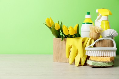 Photo of Spring cleaning. Detergents, supplies and tulips on white wooden table against green background, space for text