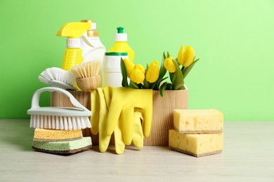 Photo of Spring cleaning. Detergents, supplies and tulips on white wooden table against green background