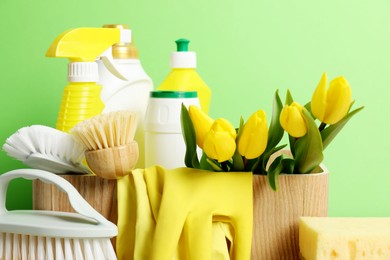 Photo of Spring cleaning. Detergents, supplies and tulips on green background, closeup