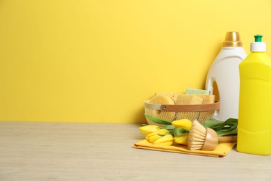 Photo of Spring cleaning. Detergents, supplies and tulips on white wooden table against yellow background, space for text