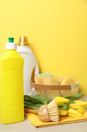 Photo of Spring cleaning. Detergents, supplies and tulips on white wooden table against yellow background