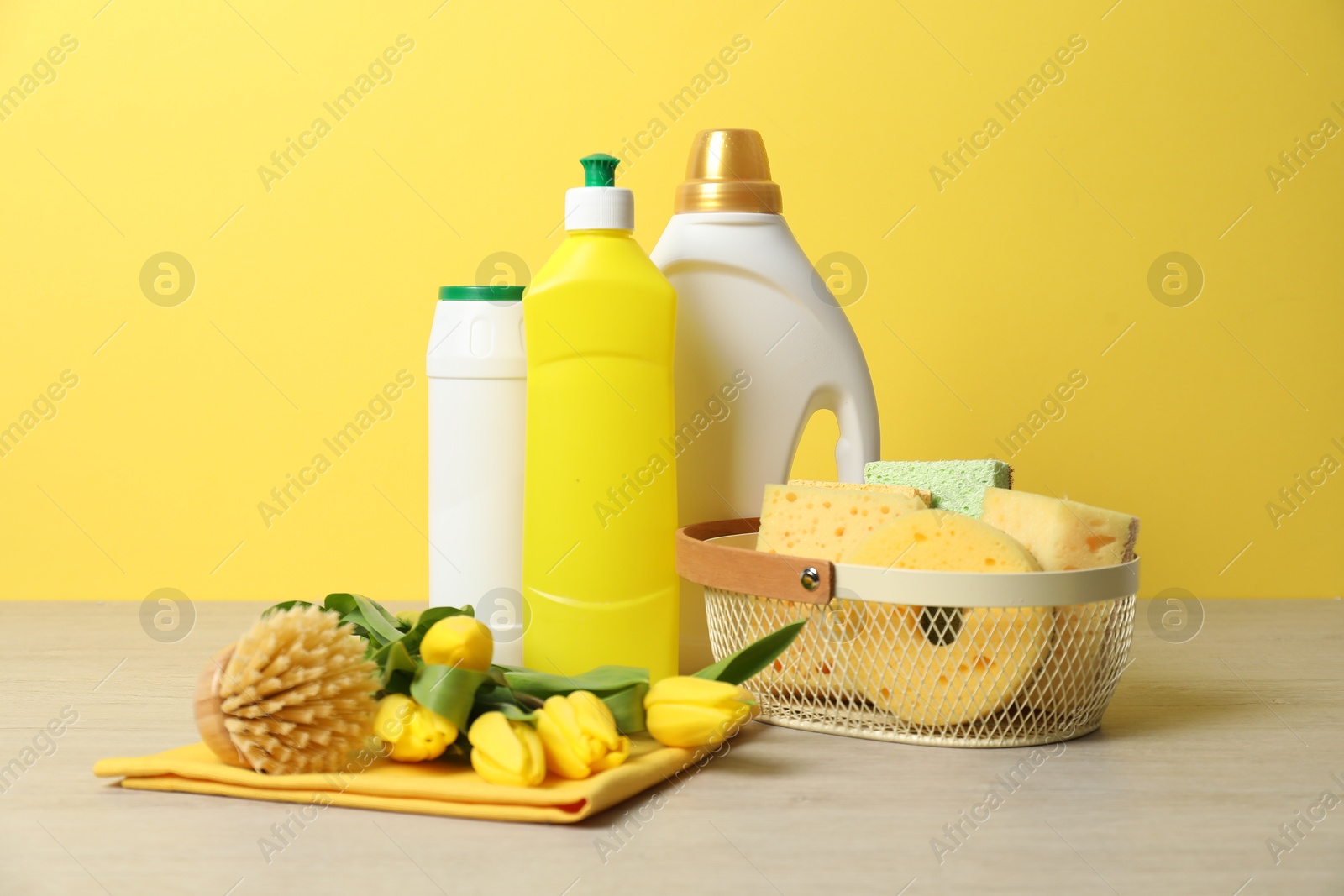 Photo of Spring cleaning. Detergents, supplies and tulips on white wooden table against yellow background