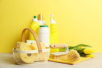 Photo of Spring cleaning. Detergents, supplies and tulips on white wooden table against yellow background