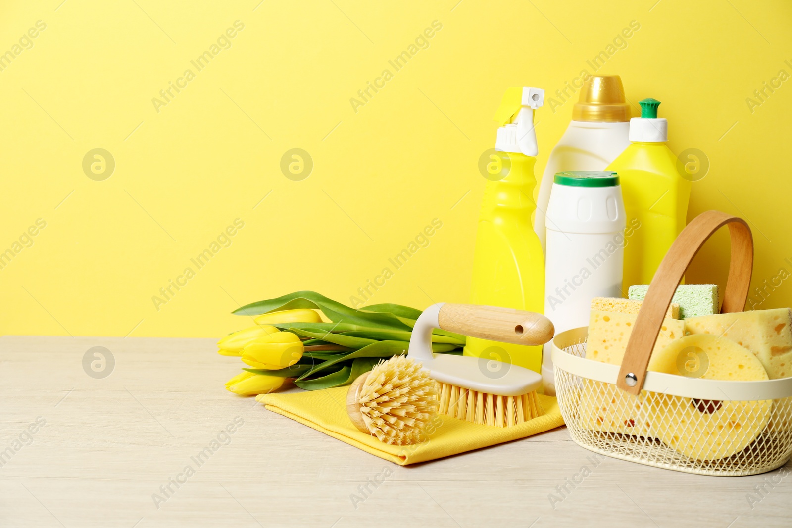 Photo of Spring cleaning. Detergents, supplies and tulips on white wooden table against yellow background, space for text