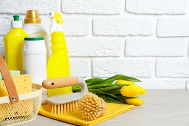 Photo of Spring cleaning. Detergents, supplies and tulips on white wooden table against brick wall, space for text