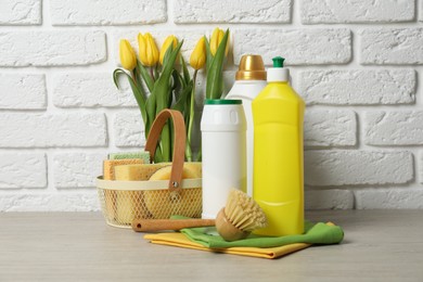 Photo of Spring cleaning. Detergents, supplies and tulips on white wooden table against brick wall