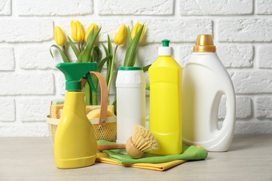 Photo of Spring cleaning. Detergents, supplies and tulips on white wooden table against brick wall