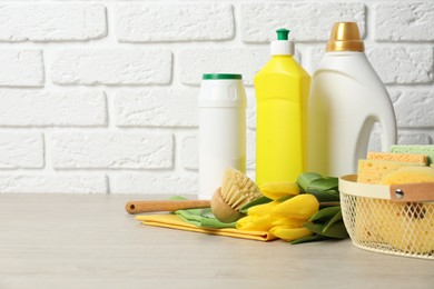 Photo of Spring cleaning. Detergents, supplies and tulips on white wooden table against brick wall, space for text