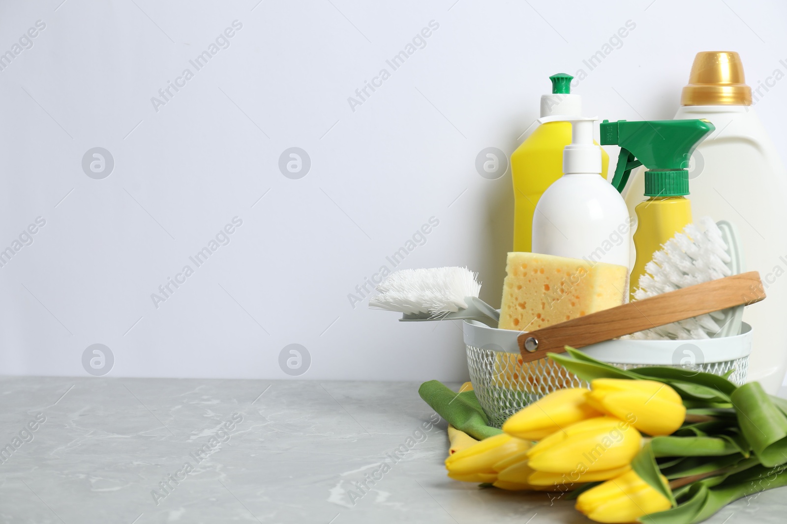 Photo of Spring cleaning. Detergents, supplies and tulips on light grey table against white background, space for text