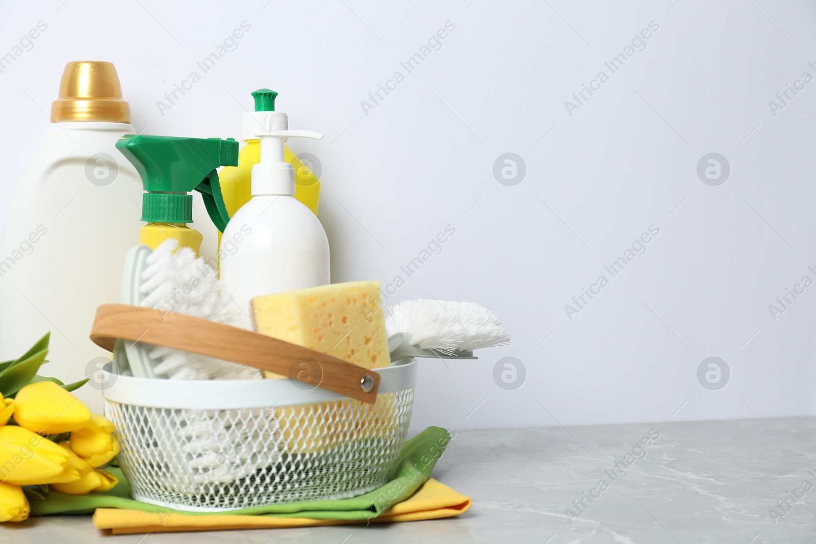 Photo of Spring cleaning. Detergents, supplies and tulips on light grey table against white background, space for text