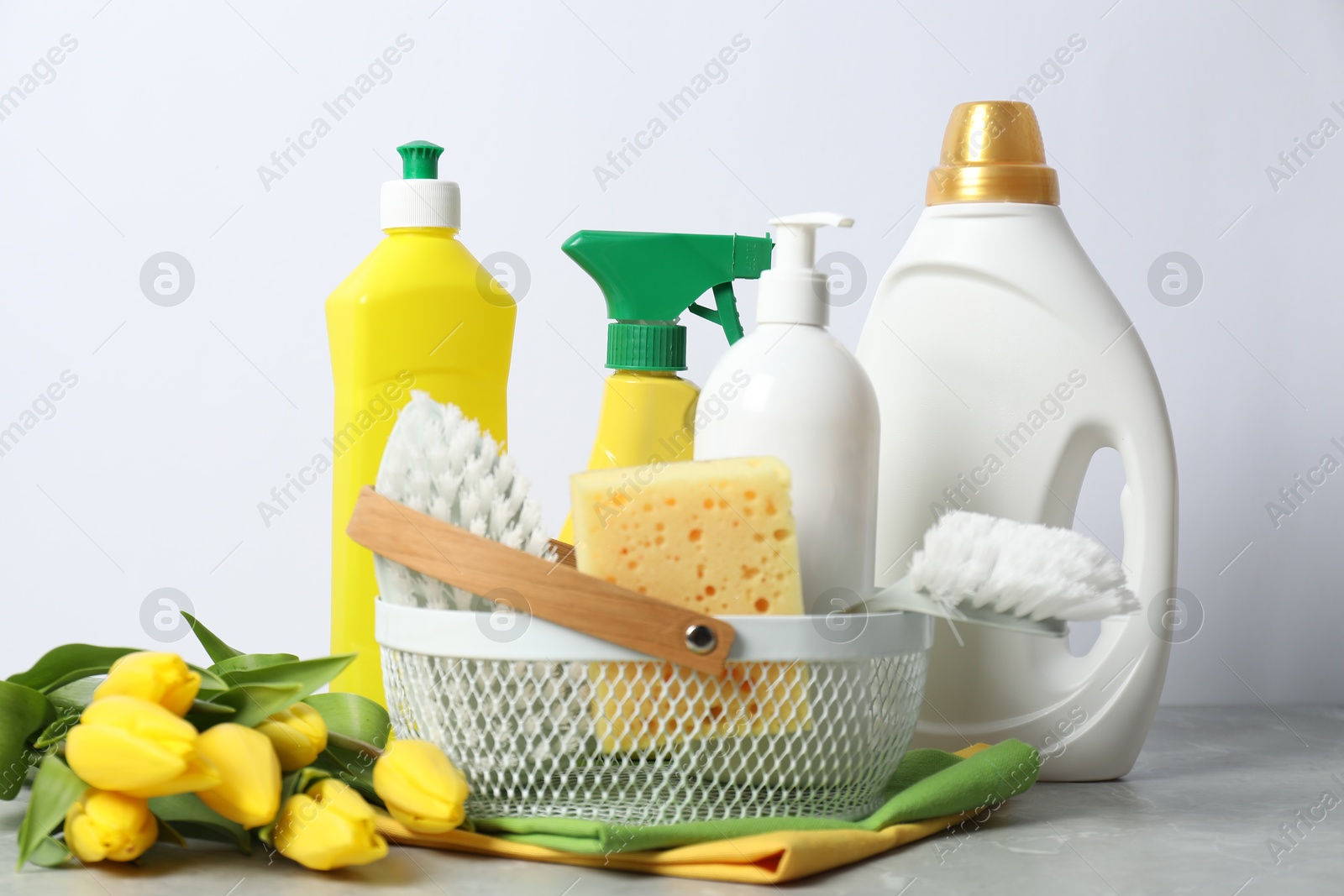 Photo of Spring cleaning. Detergents, supplies and tulips on light grey table against white background