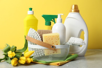 Photo of Spring cleaning. Detergents, supplies and tulips on light grey table against yellow background