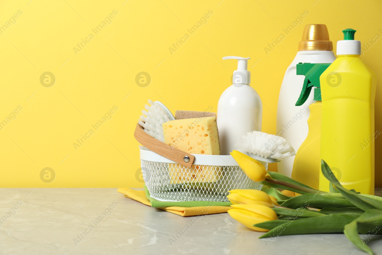 Photo of Spring cleaning. Detergents, supplies and tulips on light grey table against yellow background, space for text