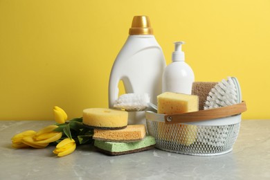 Photo of Spring cleaning. Detergents, supplies and tulips on light grey table against yellow background