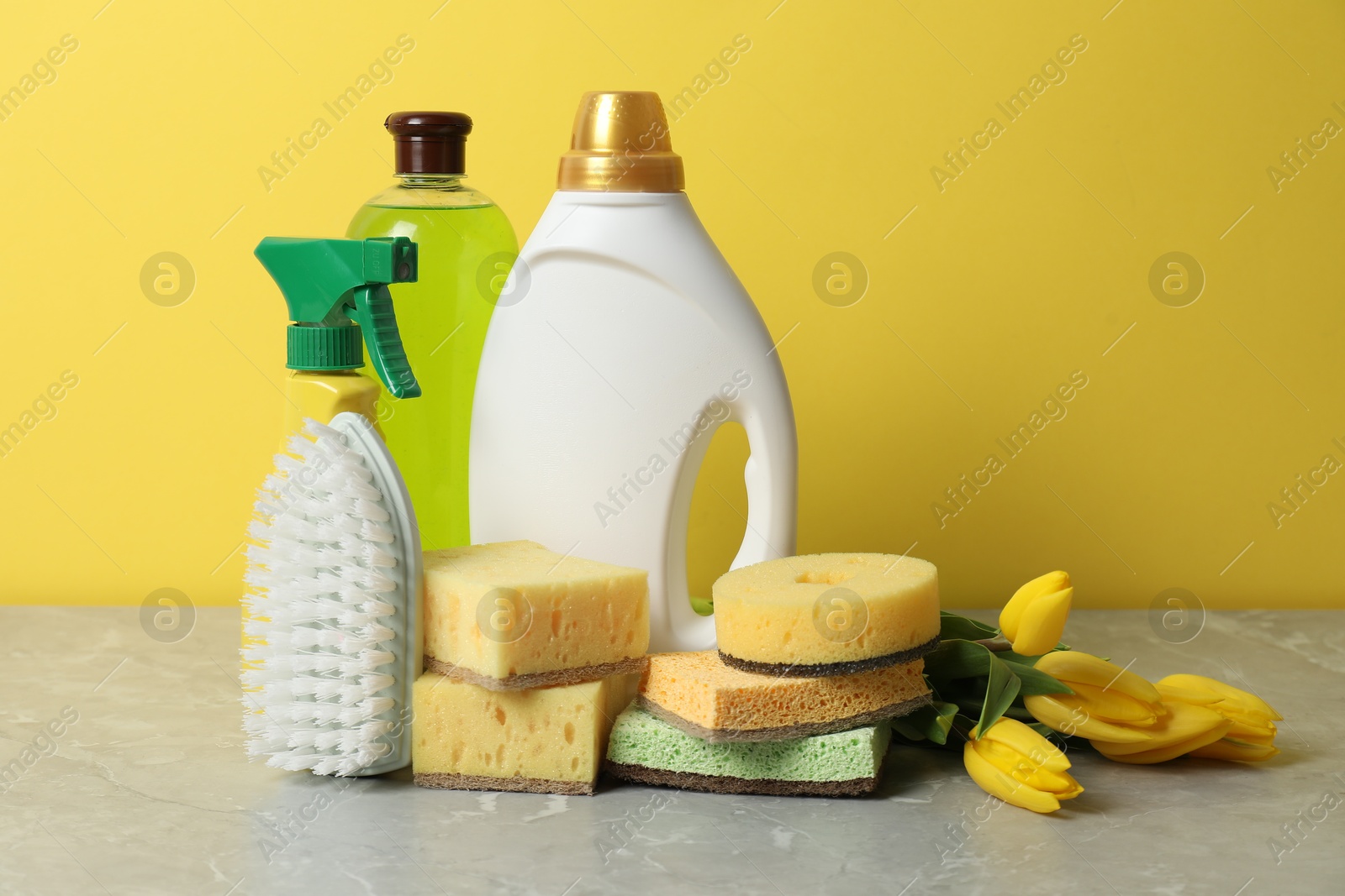 Photo of Spring cleaning. Detergents, supplies and tulips on light grey table against yellow background