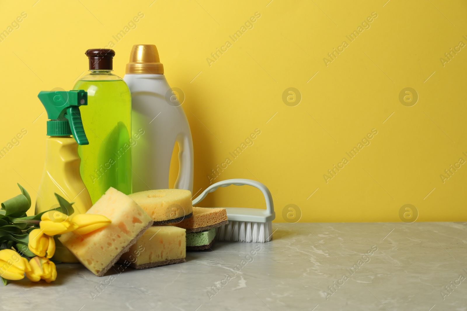 Photo of Spring cleaning. Detergents, supplies and tulips on light grey table against yellow background, space for text