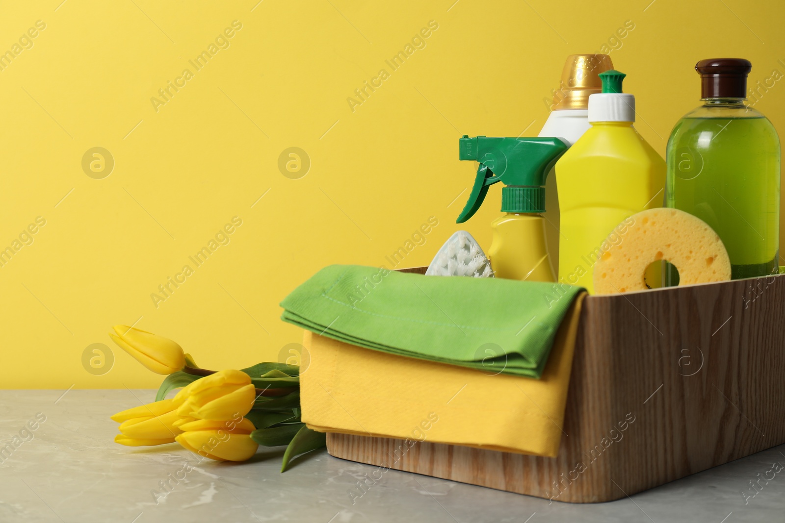 Photo of Spring cleaning. Detergents, supplies and tulips on light grey table against yellow background