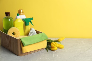 Photo of Spring cleaning. Detergents, supplies and tulips on light grey table against yellow background, space for text