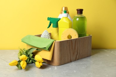 Photo of Spring cleaning. Detergents, supplies and tulips on light grey table against yellow background