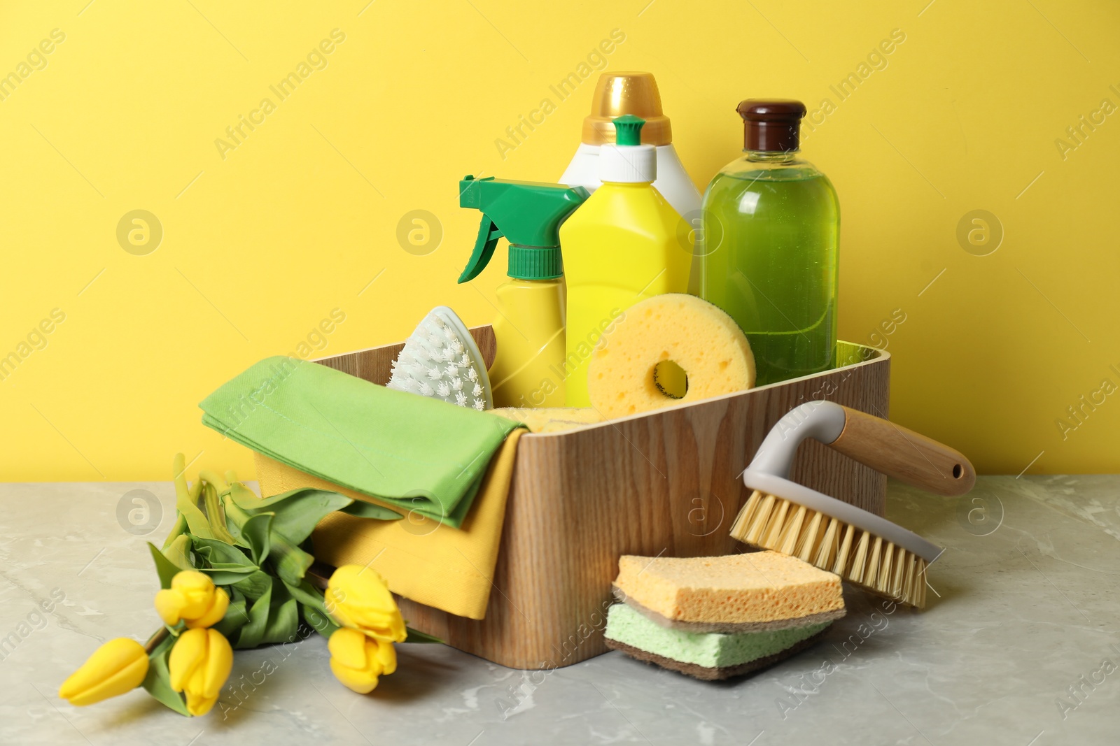 Photo of Spring cleaning. Detergents, supplies and tulips on light grey table against yellow background