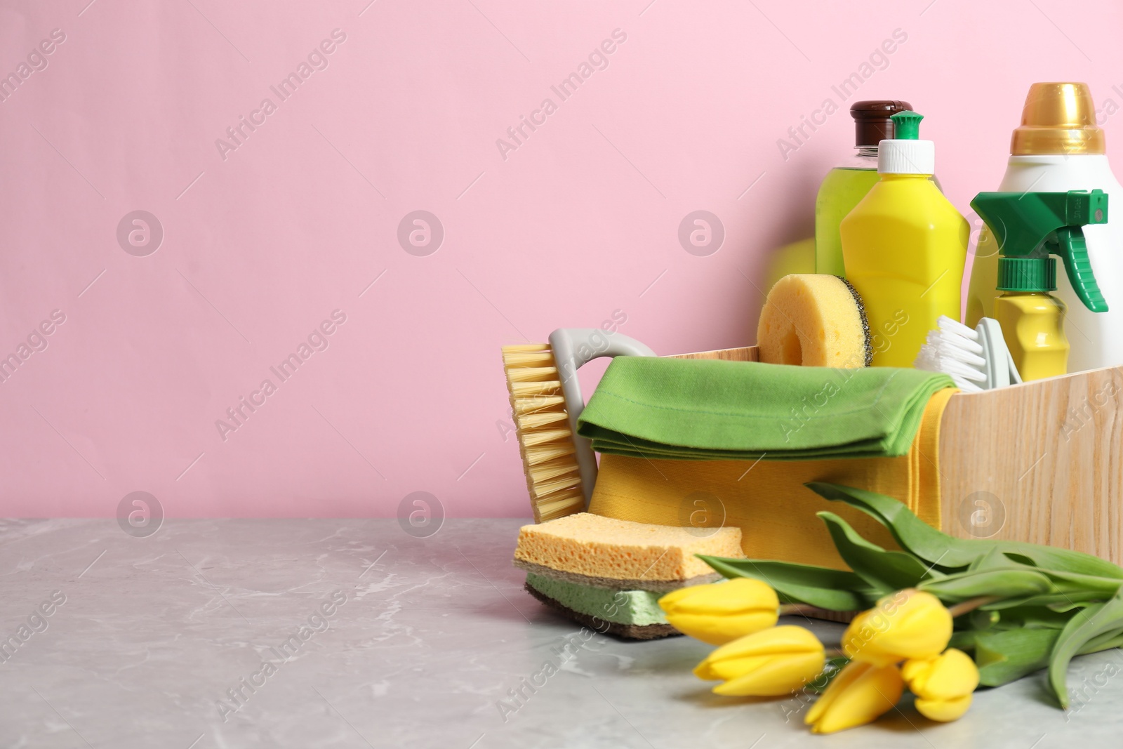 Photo of Spring cleaning. Detergents, supplies and tulips on light grey table against pink background, space for text