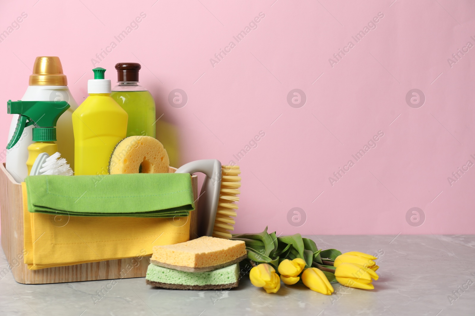 Photo of Spring cleaning. Detergents, supplies and tulips on light grey table against pink background, space for text