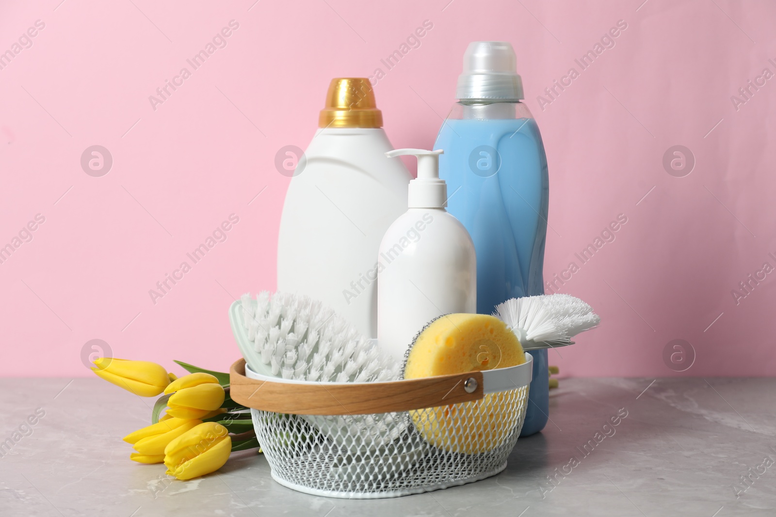 Photo of Spring cleaning. Detergents, supplies and tulips on light grey table against pink background