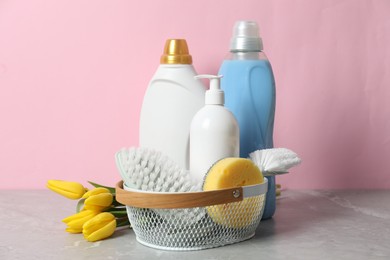 Photo of Spring cleaning. Detergents, supplies and tulips on light grey table against pink background