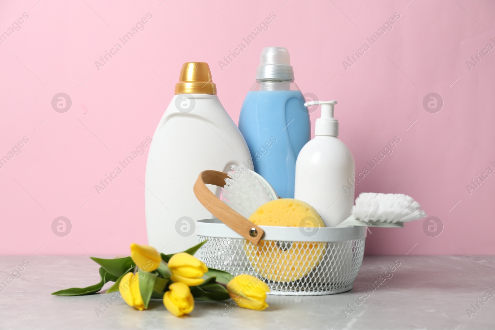 Photo of Spring cleaning. Detergents, supplies and tulips on light grey table against pink background