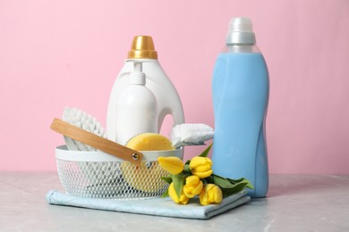 Photo of Spring cleaning. Detergents, supplies and tulips on light grey table against pink background