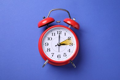 Daylight saving time. Red alarm clock on blue background, top view. Highlighted area showing time change by one hour forward